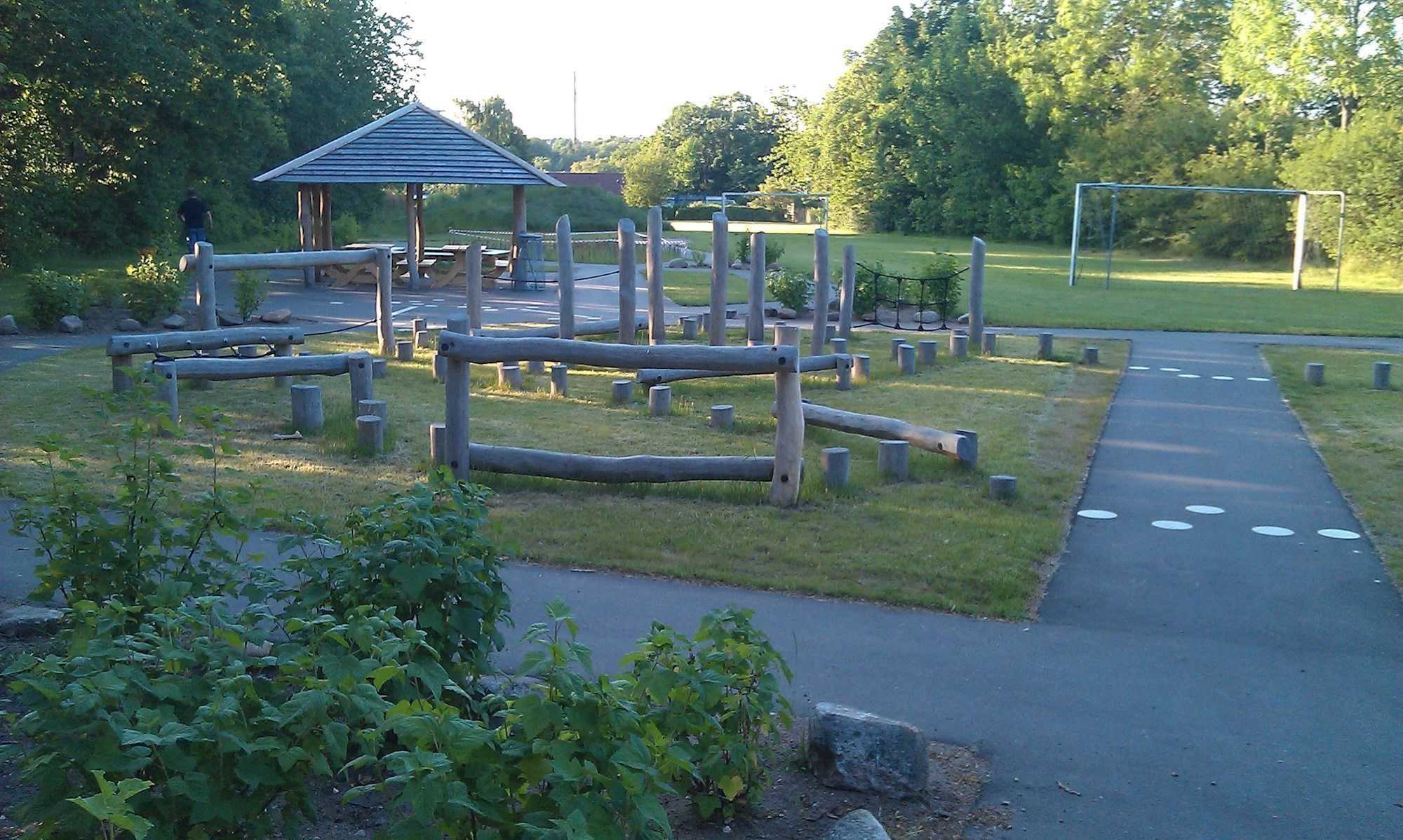 Legeplads med mange klatreredskaber i træ. Fodboldmål i baggrunden